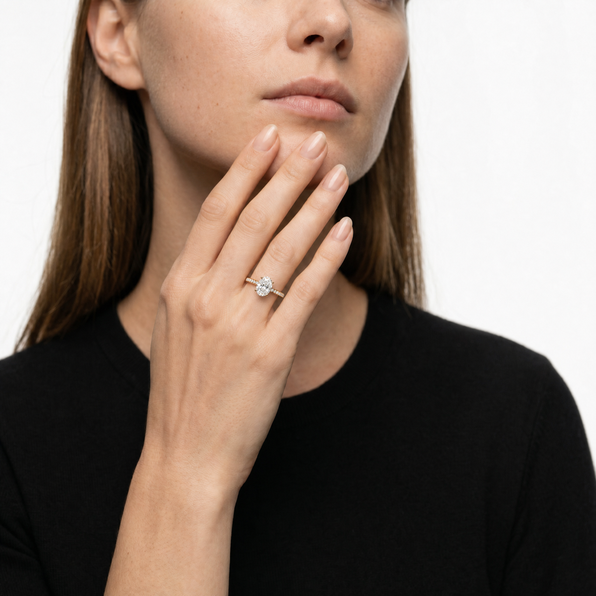 A high-fashion shot of a Raul Diamonds oval cut engagement ring on a model's hand, showcasing the brilliant oval stone, hidden halo, and slim pavé-set diamond band.