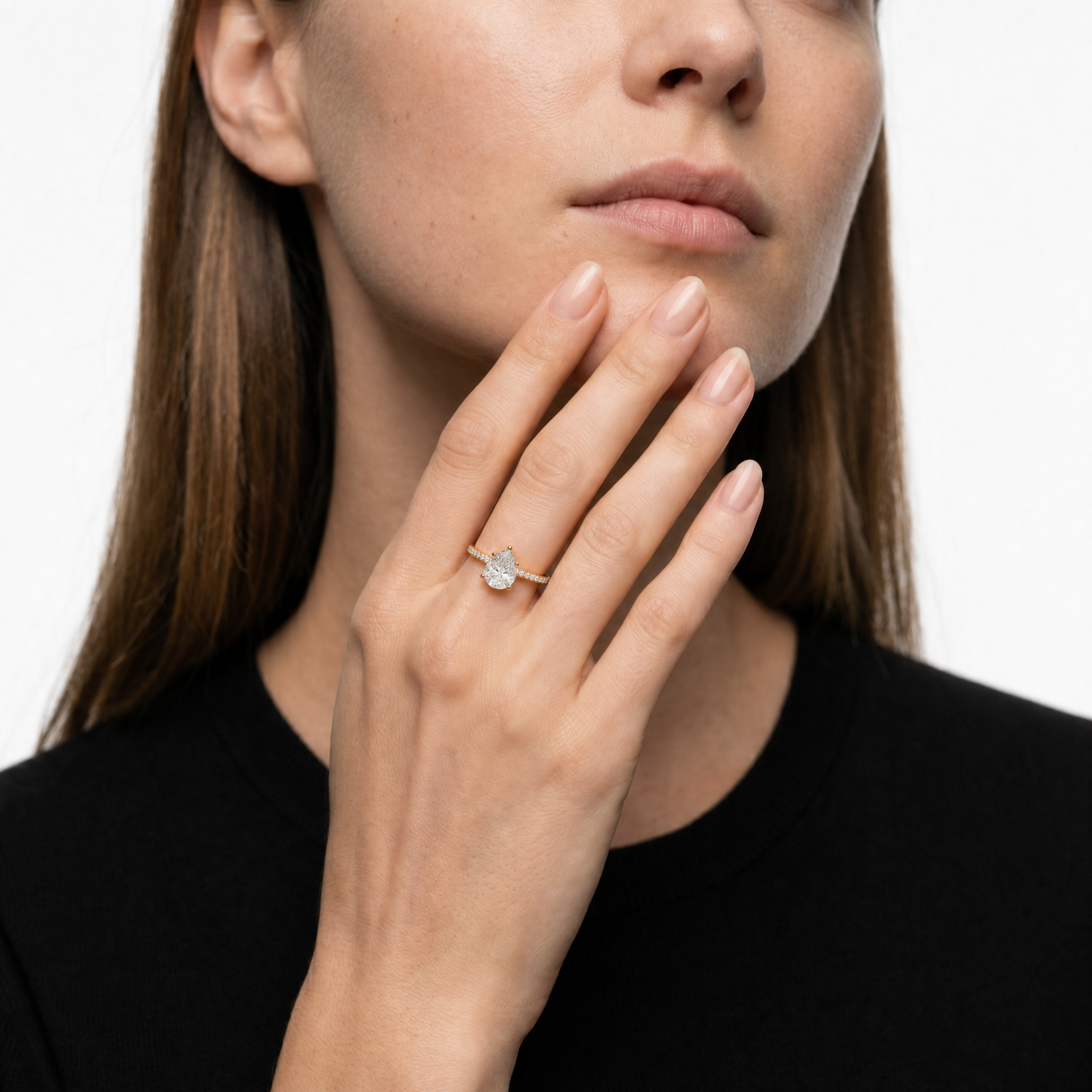 A luxury lifestyle shot featuring a Raul Diamonds pear-cut engagement ring on a model's hand, highlighting the elegant teardrop shape and the sparkling hidden halo setting.