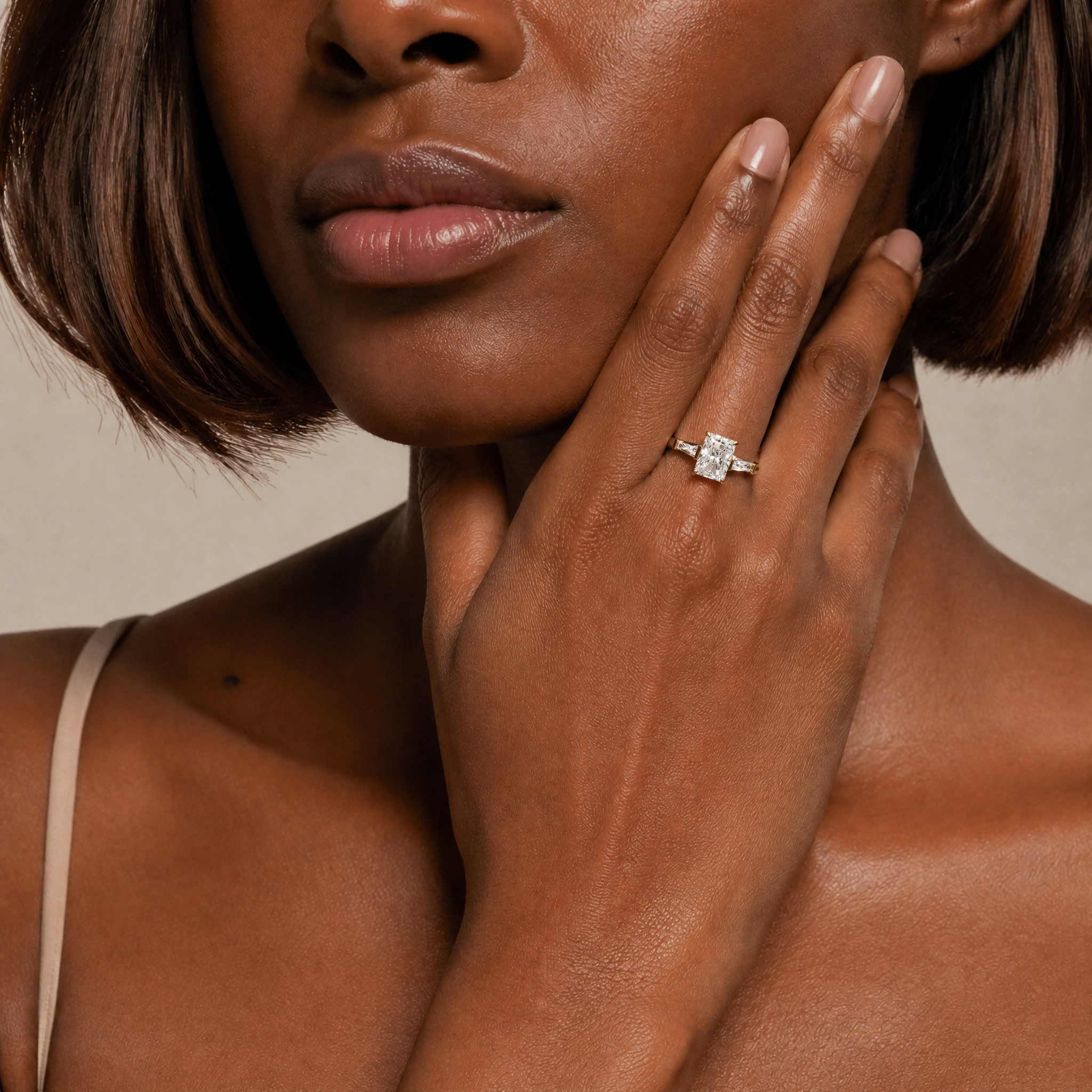 A close-up of a model's hand showcasing a Raul Diamonds radiant-cut diamond engagement ring with tapered baguette side stones, emphasizing its elegant sparkle and premium craftsmanship.