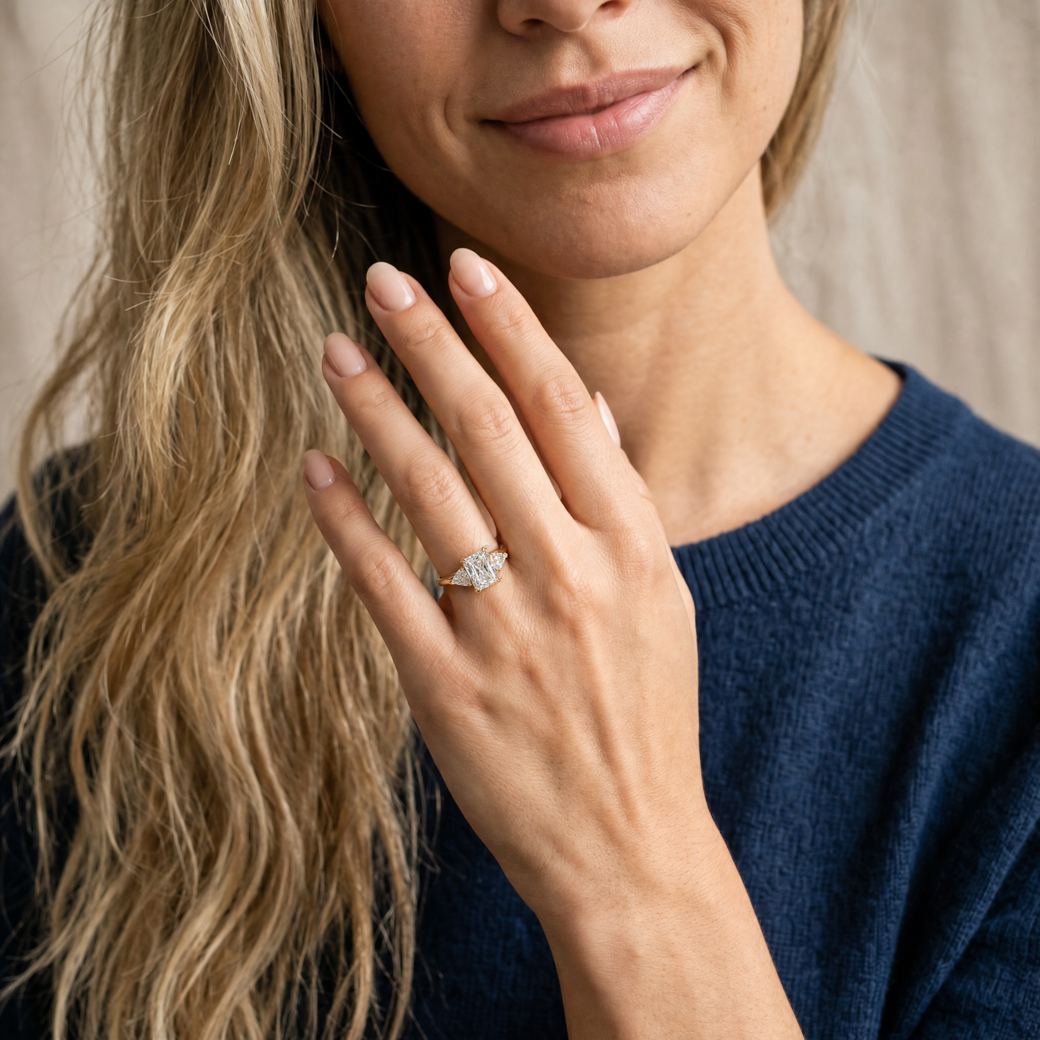 A close-up lifestyle photograph of a hand wearing a Raul Diamonds radiant-cut three-stone engagement ring, showcasing the complex facet pattern and brilliant sparkle against a soft background