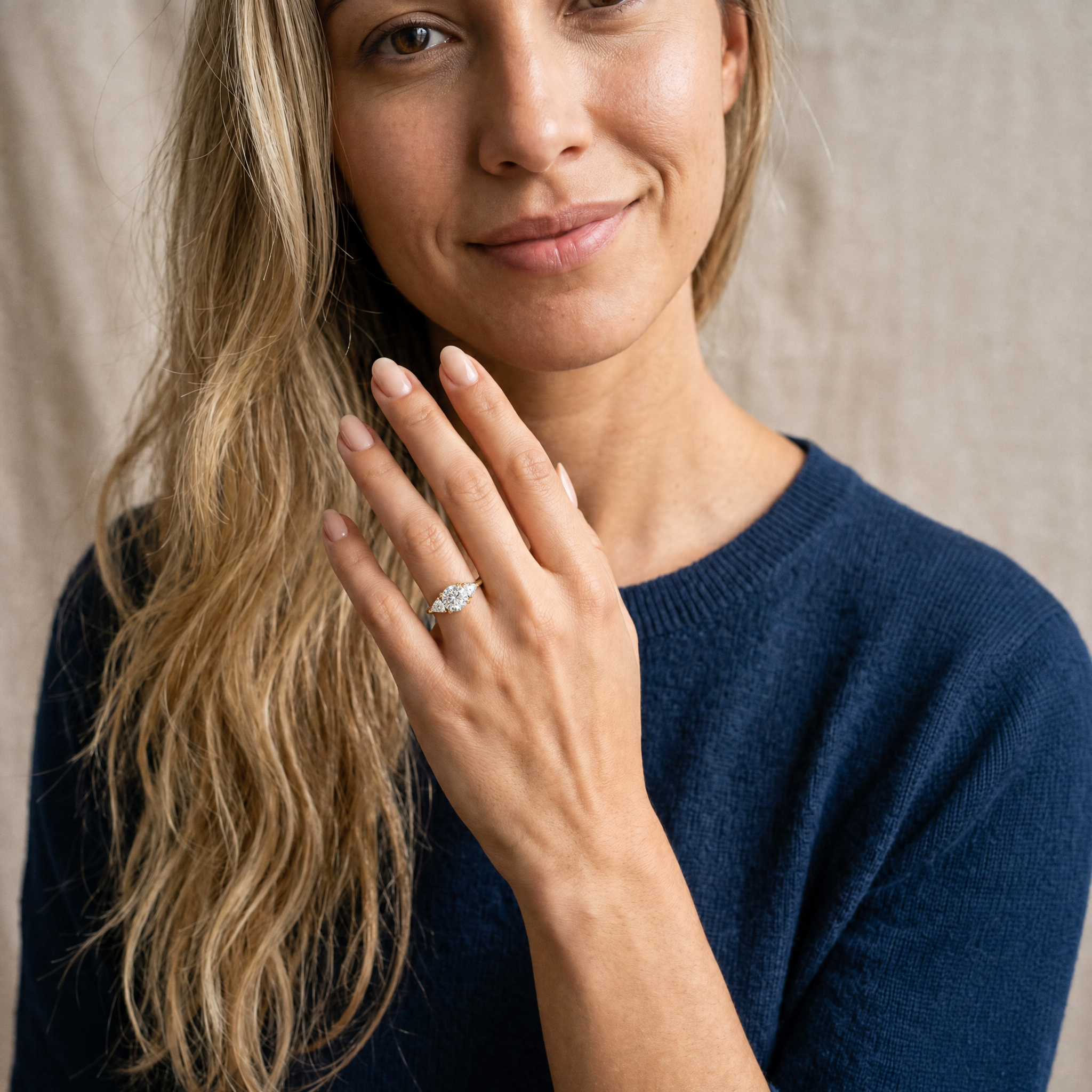 A high-resolution lifestyle shot of a hand wearing a Raul Diamonds round brilliant three-stone engagement ring, showcasing the classic silhouette and exceptional fire of the lab-grown diamonds.