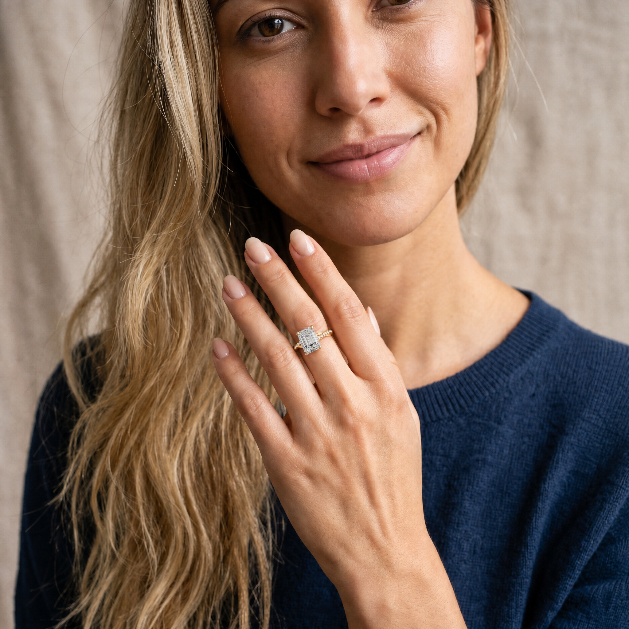 A lifestyle perspective of a model wearing a Raul Diamonds emerald cut engagement ring, showcasing the elongated diamond shape and elegant pavé twist band on a finger