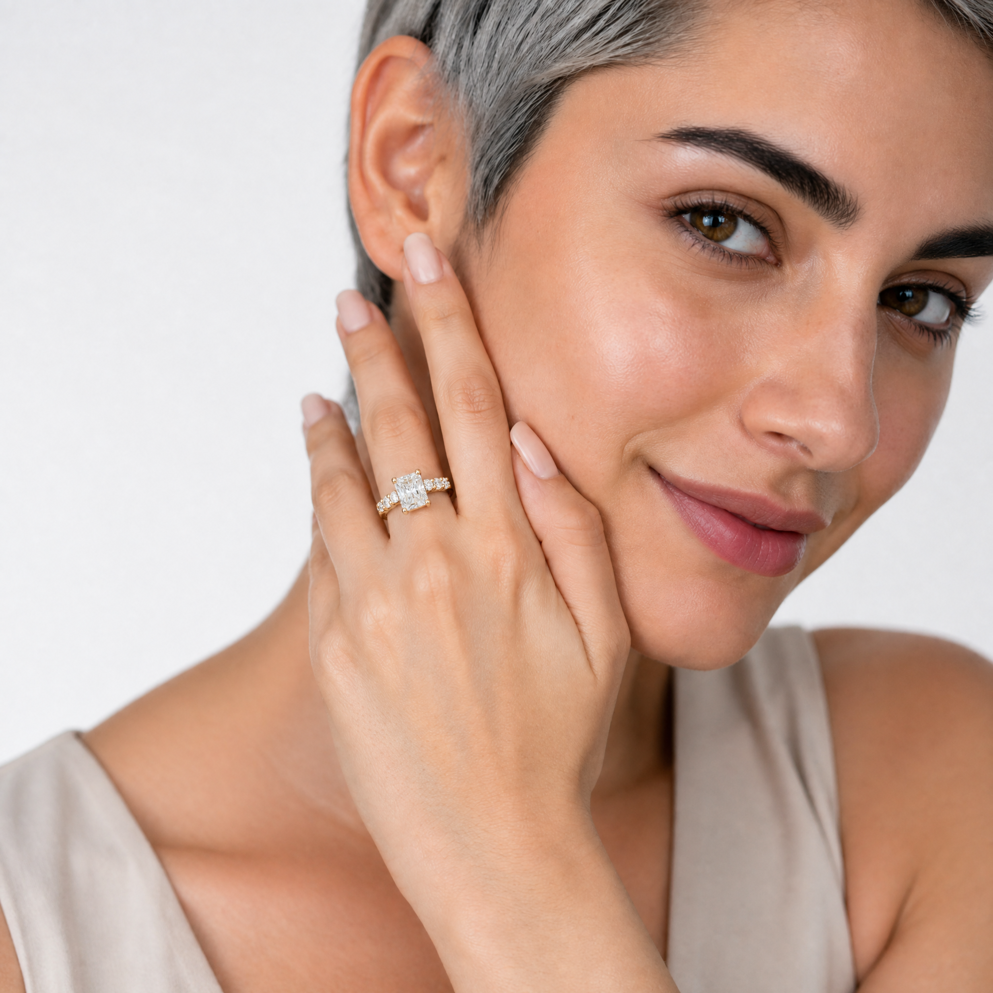 A close-up of a model wearing a Raul Diamonds radiant-cut diamond ring, showcasing the high-set center stone and the elegant scalloped profile of the eternity band