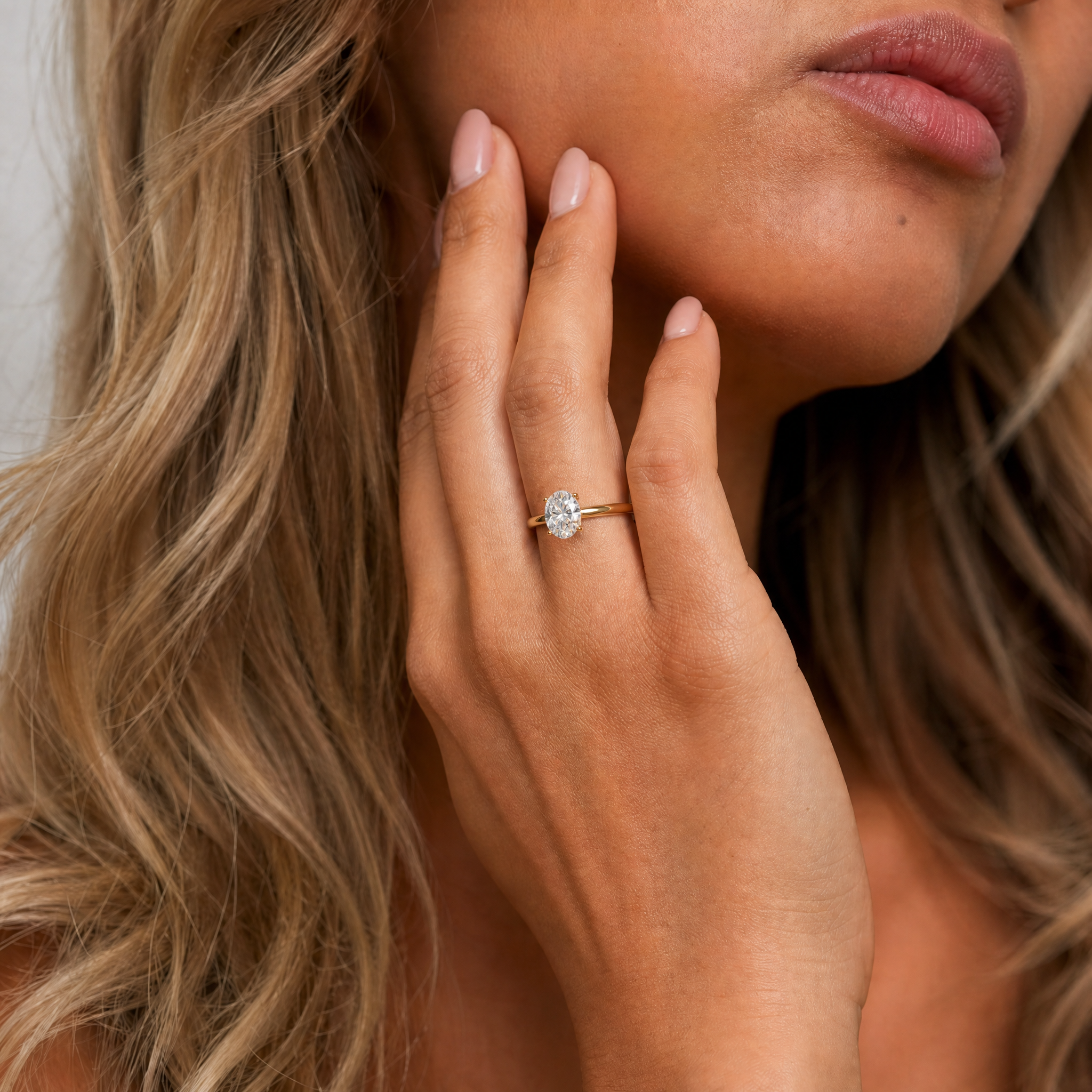 A close-up of a model wearing a Raul Diamonds oval cut solitaire engagement ring, showcasing how the elegant elongated diamond shape flatters the hand on a polished gold band