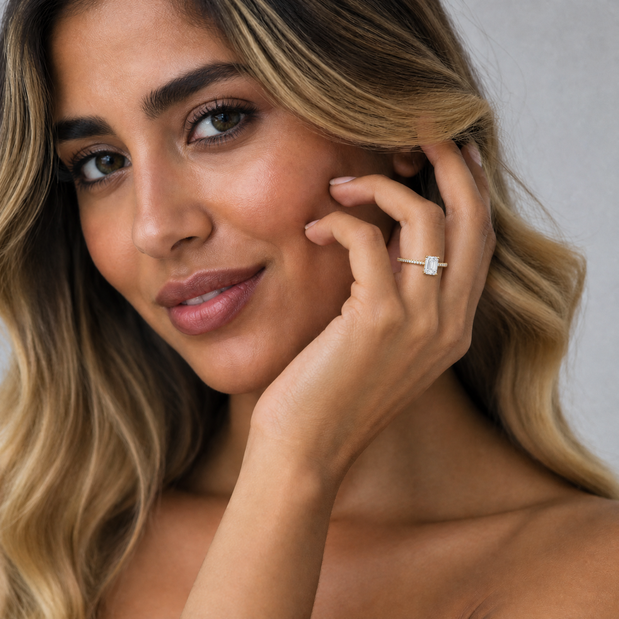 Elegantly posed hand wearing a Raul Diamonds emerald cut engagement ring, showcasing the elongated step-cut diamond and sparkling hidden halo against a luxury backdrop