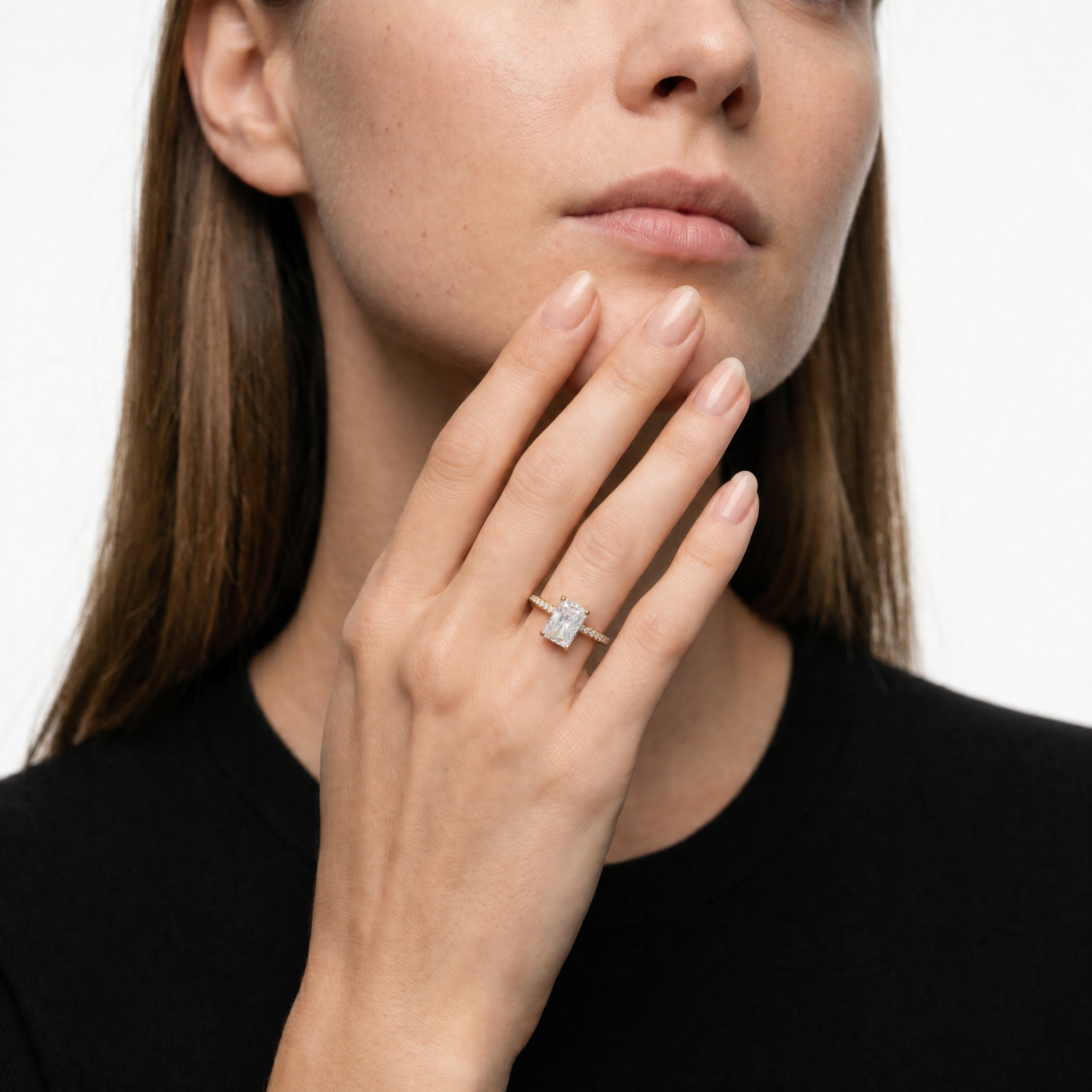 Hand of a model wearing a Raul Diamonds radiant cut engagement ring, showcasing the rectangular brilliant-cut diamond, signature hidden halo, and a pavé-set diamond band