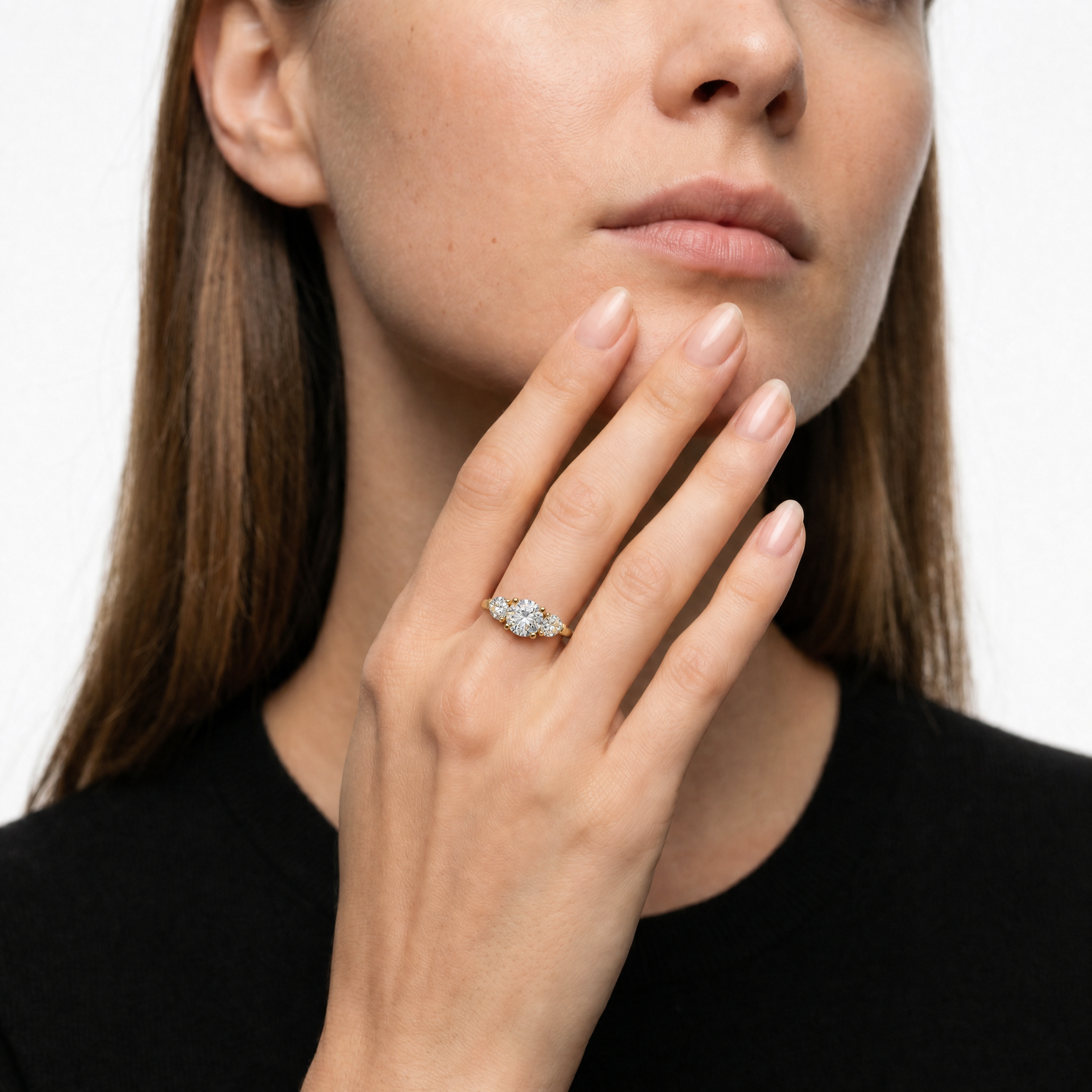 Luxury model wearing Raul Diamonds round cut three stone lab grown diamond engagement ring featuring pear shaped side diamonds and elegant yellow gold band for timeless bridal style
