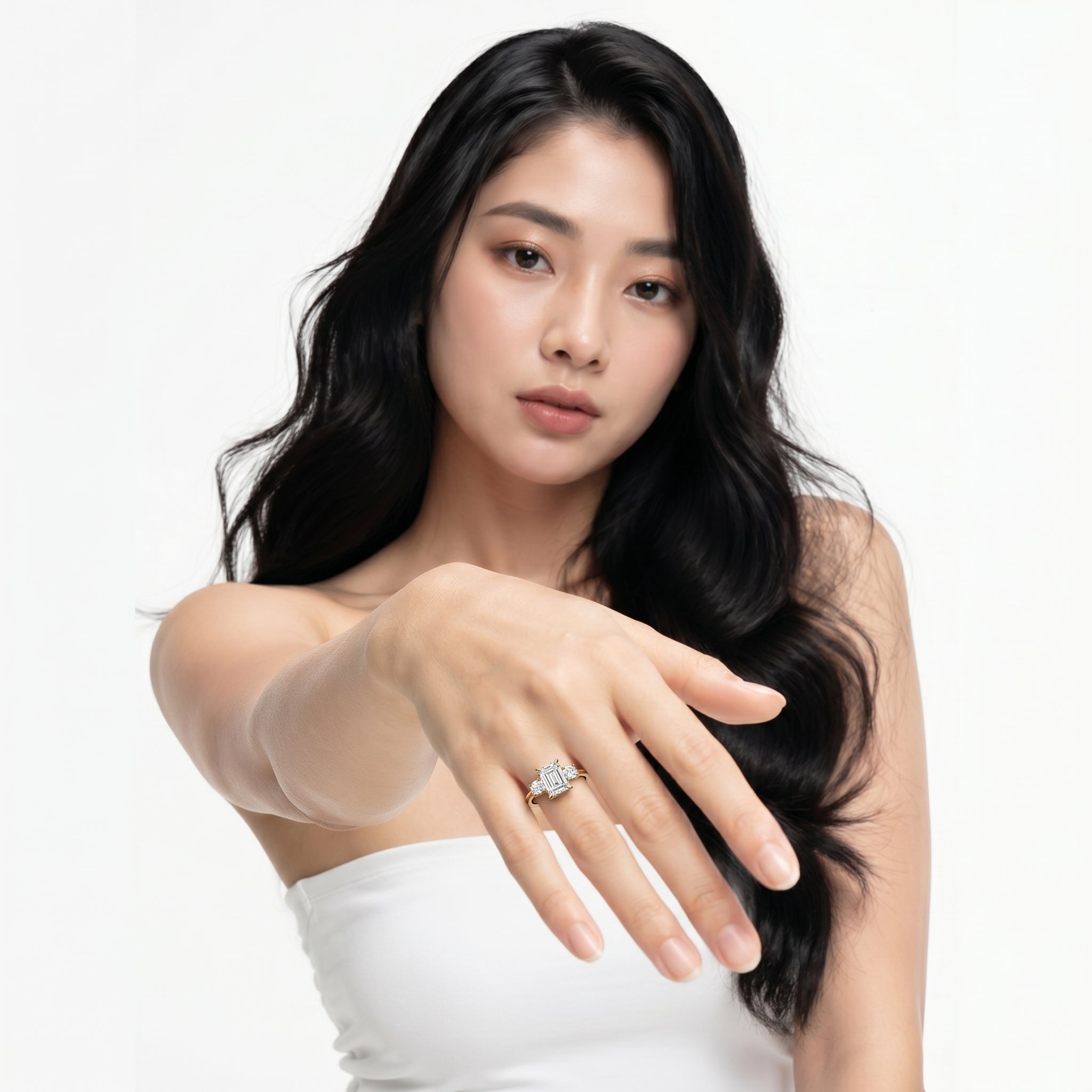 A close-up lifestyle shot of the Elena Trilogy ring by Raul Diamonds, featuring a center emerald cut diamond flanked by two round brilliant diamonds on a polished gold band.