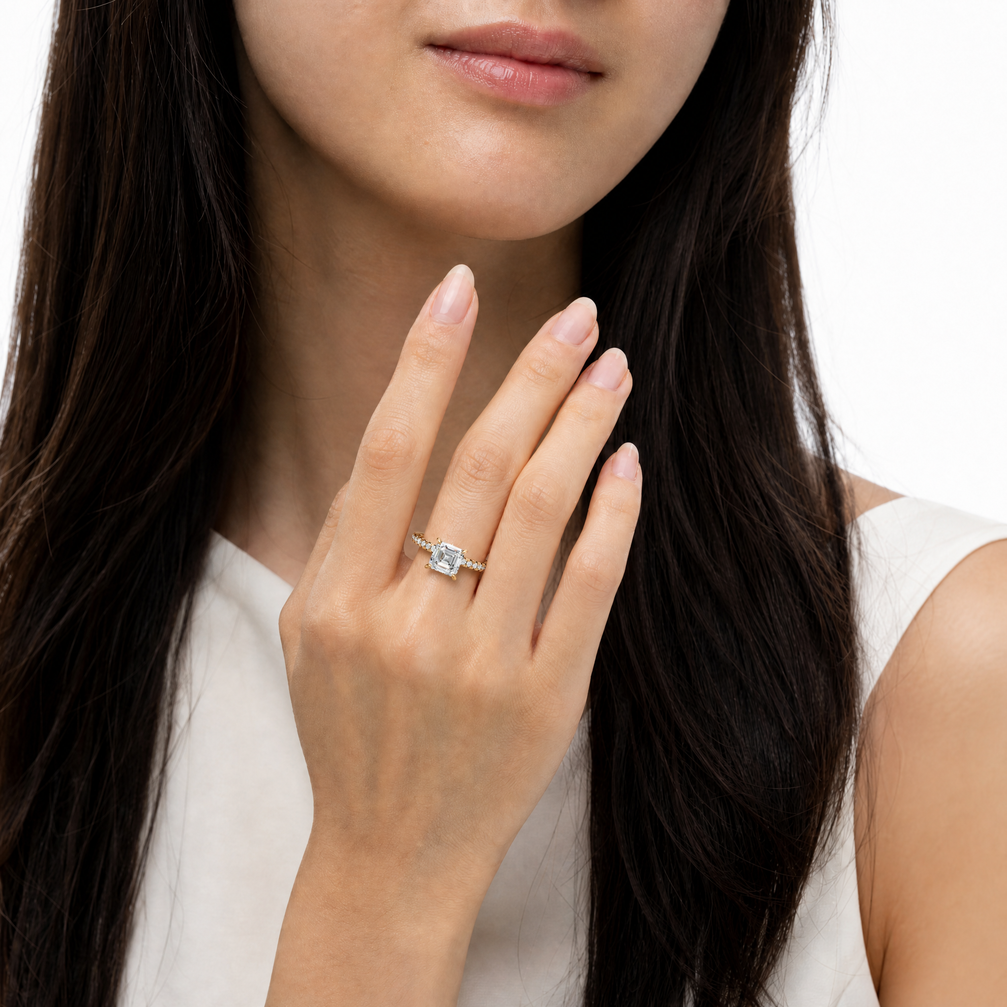 Elegant female hand wearing a Raul Diamonds Asscher cut diamond engagement ring with a thin pave band and hidden halo setting.