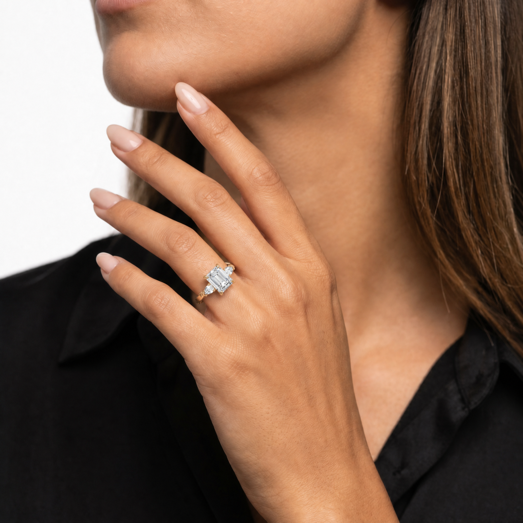 Elegant model wearing the Raul Diamonds Seraphina emerald cut diamond ring with pear side stones in 18k yellow gold, showcasing a sophisticated hand-jewelry look