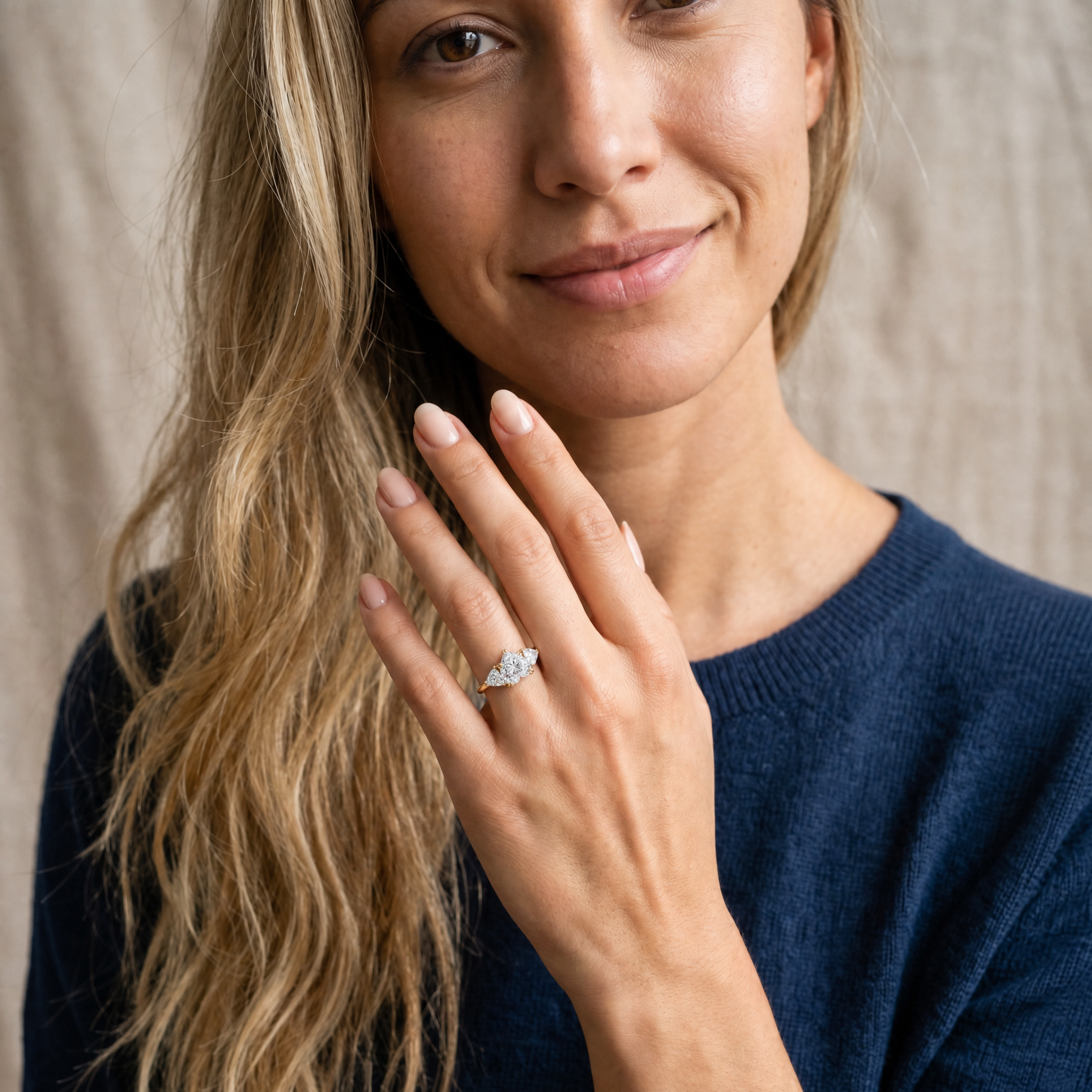 A close-up lifestyle shot of a hand wearing a Raul Diamonds heart-shaped three-stone engagement ring, showcasing the brilliance and scale of the center diamond in a natural setting.