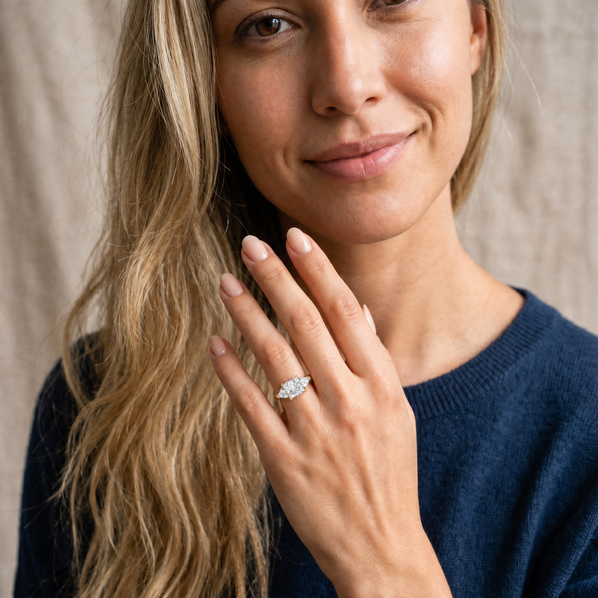 A hand modeling a Raul Diamonds princess-cut three-stone engagement ring, showcasing the bold square shape and brilliant light return of the center stone