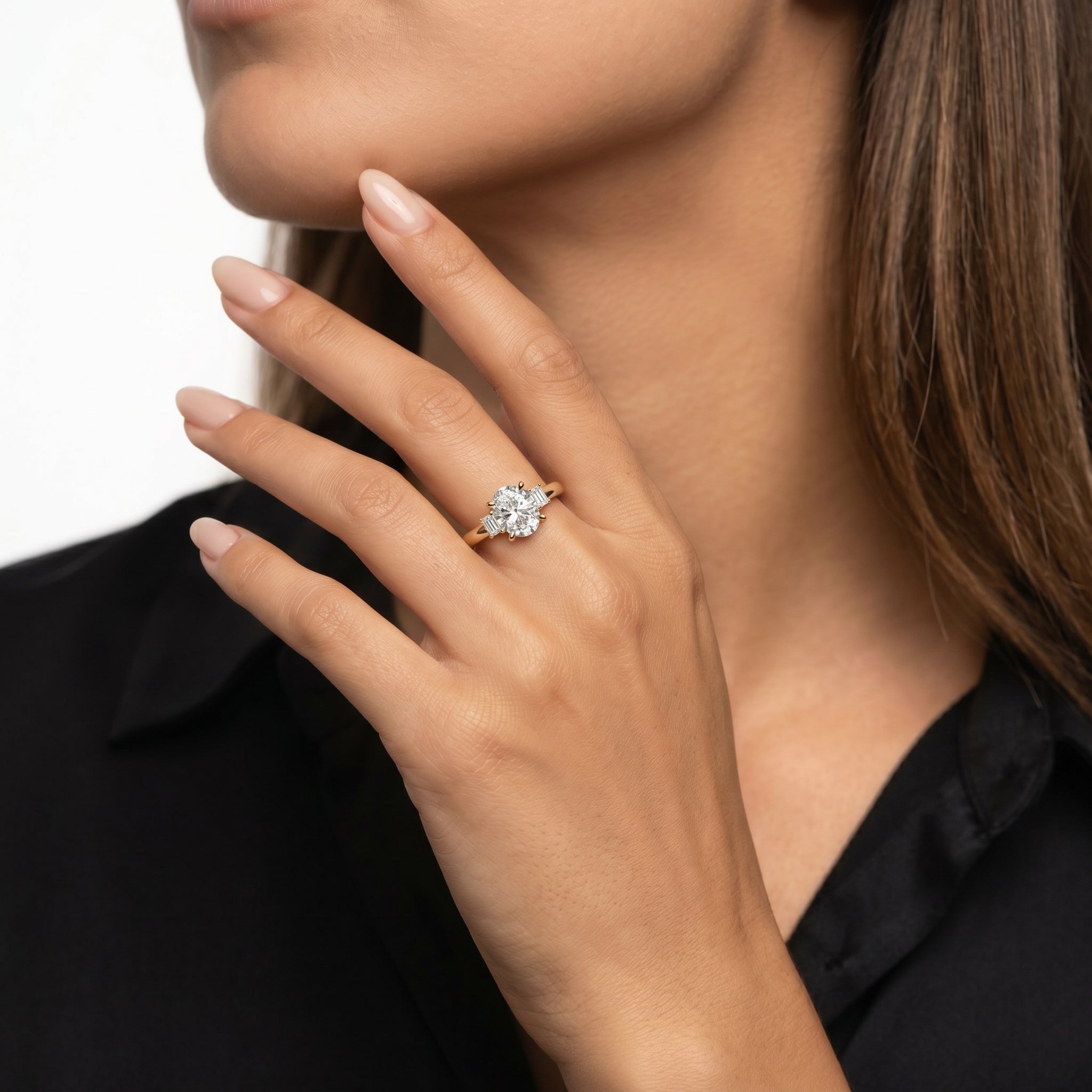 A close-up of a model's hand wearing a Raul Diamonds three-stone engagement ring featuring a large oval center diamond flanked by two emerald-cut side stones.
