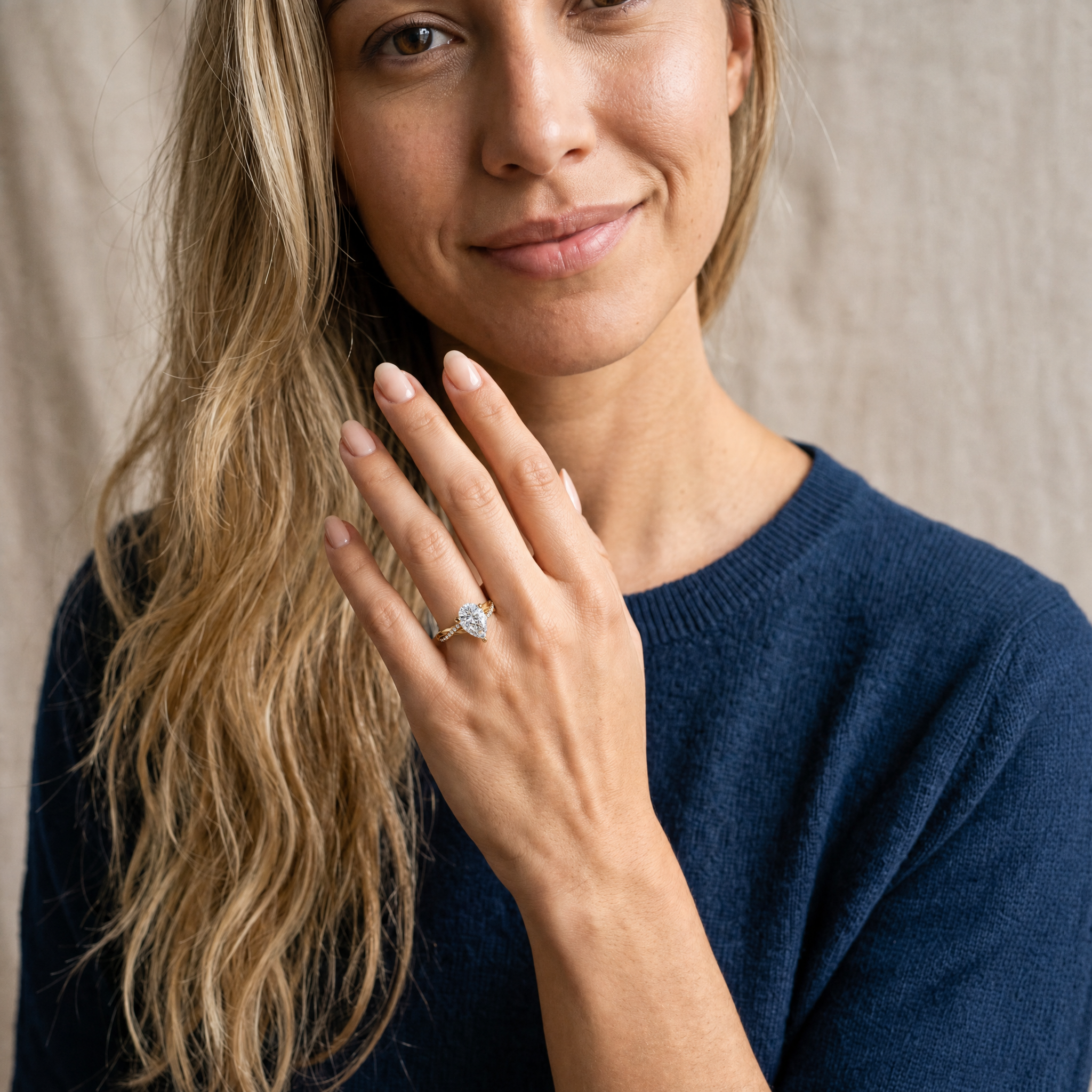 A lifestyle shot of a model wearing a Raul Diamonds pear-shaped diamond engagement ring, showcasing the elegant teardrop silhouette and the shimmering twisted pavé band on a finger