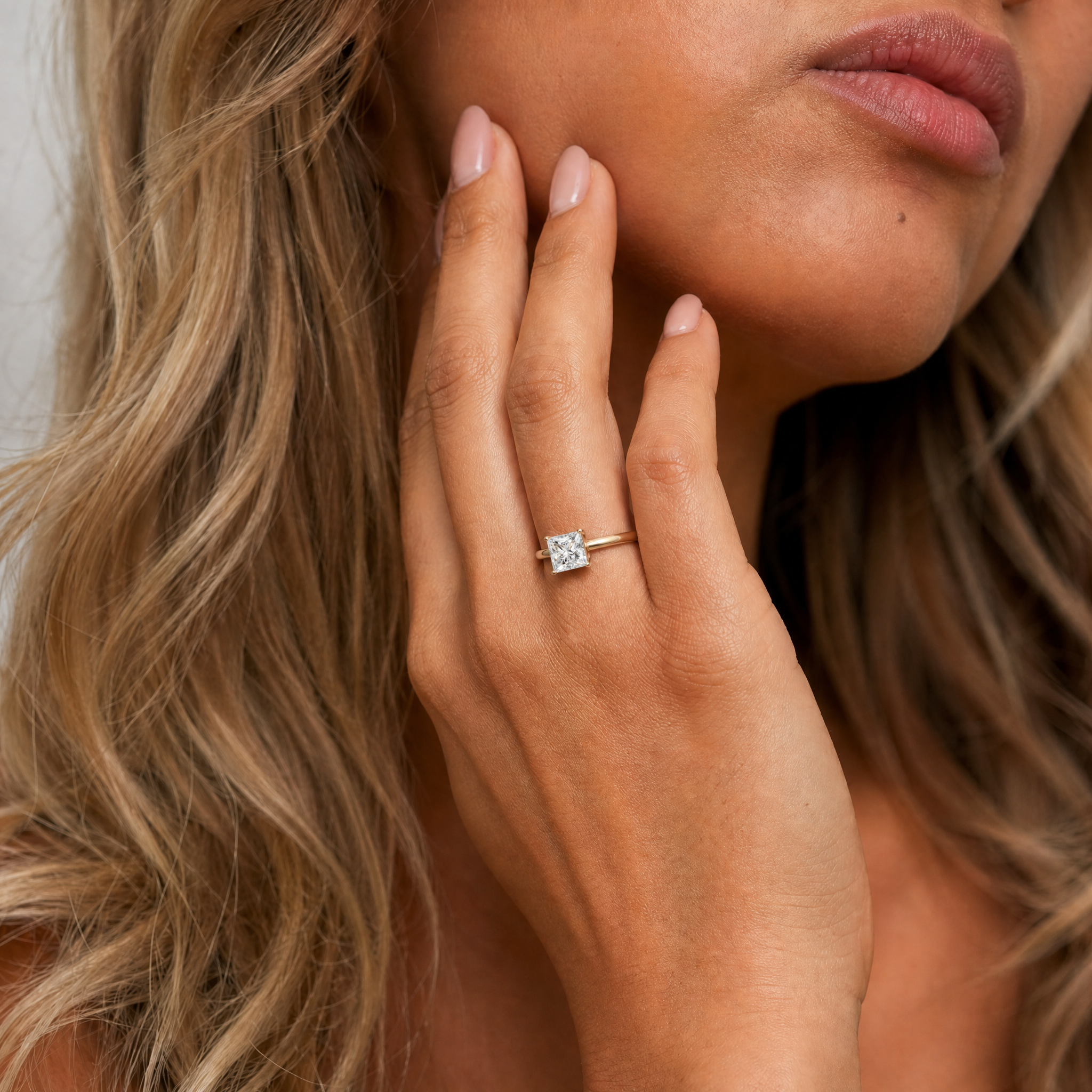 An elegant shot of a model wearing a Raul Diamonds princess cut solitaire engagement ring, highlighting the sharp, modern corners of the square diamond on a high-polish gold band