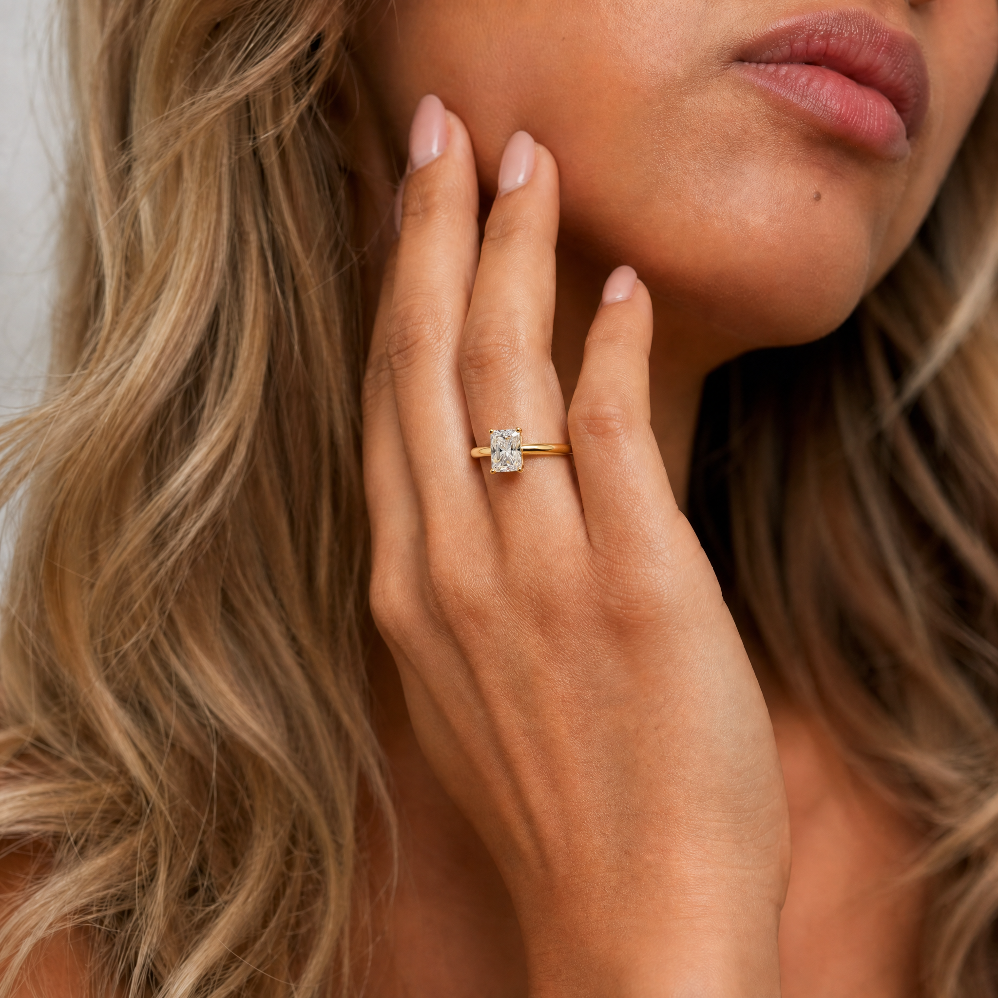 A model wearing a Raul Diamonds radiant cut solitaire engagement ring, showcasing the rectangular brilliant-cut diamond's exceptional sparkle and modern gold setting on a hand.