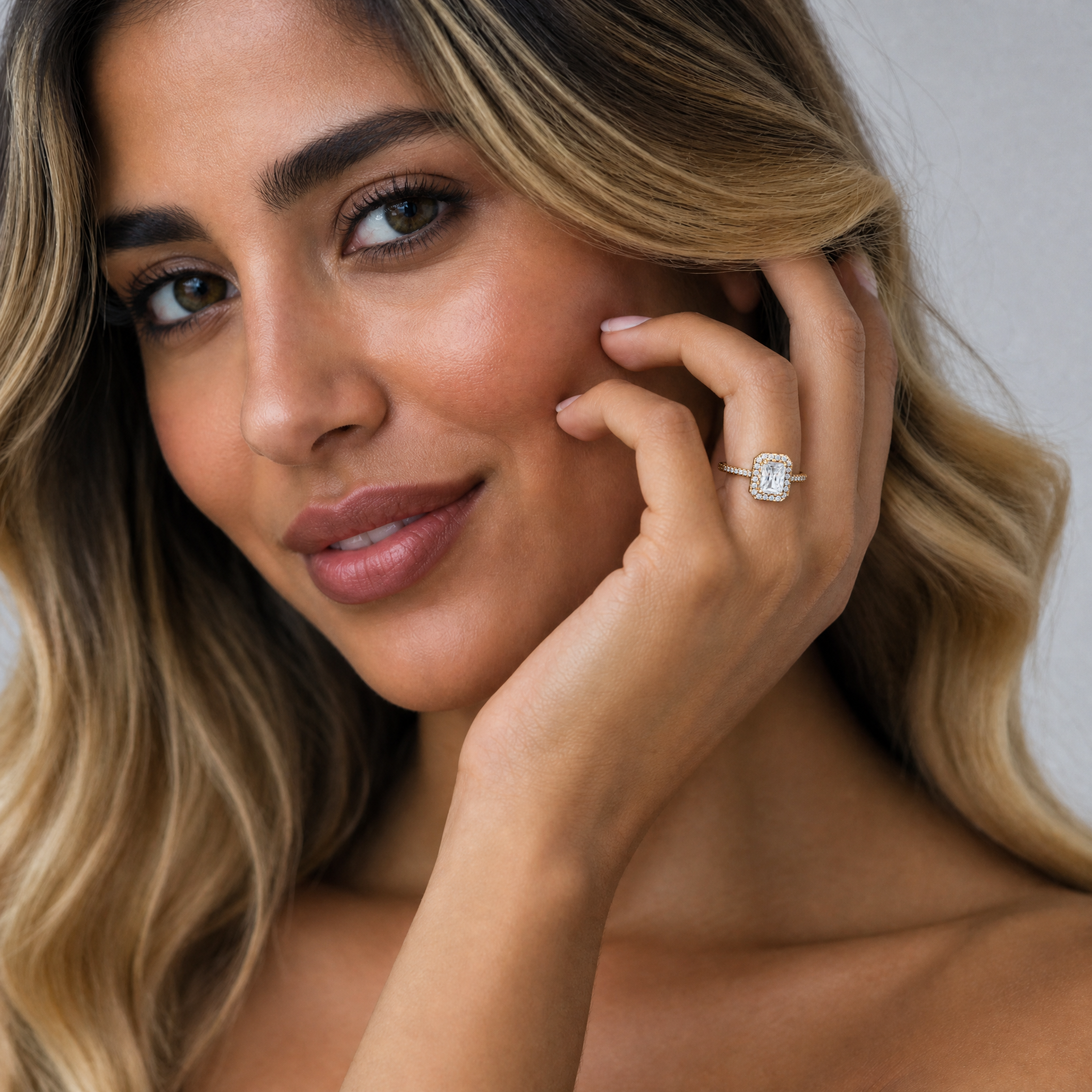 Female model wearing Raul Diamonds radiant cut halo engagement ring in yellow gold with pavé diamond band