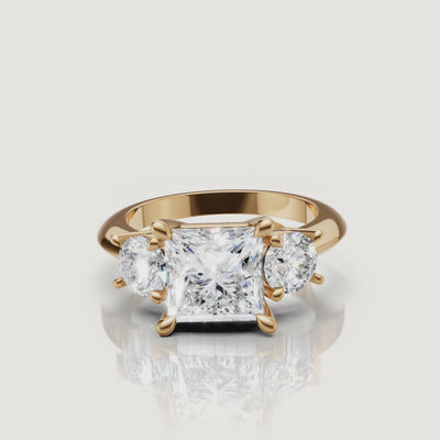 360-degree video showcase of the Raul Diamonds princess cut three-stone ring in yellow gold, highlighting the sharp geometric brilliance and fire of the round side diamonds.