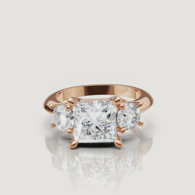 Cinematic close-up of the Victoria rose gold princess trilogy ring, focusing on the warm blush metal and the exceptional light return of the square-cut center diamond.