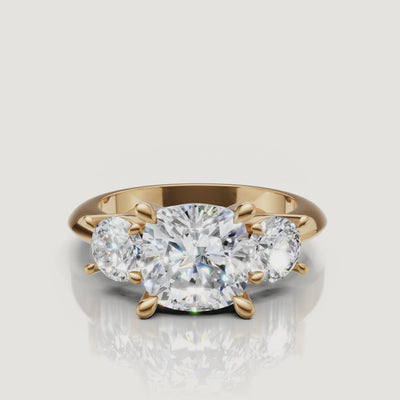 360-degree video showcase of the Raul Diamonds cushion cut three-stone ring in yellow gold, highlighting the soft pillow shape and the fire of the round side diamonds.