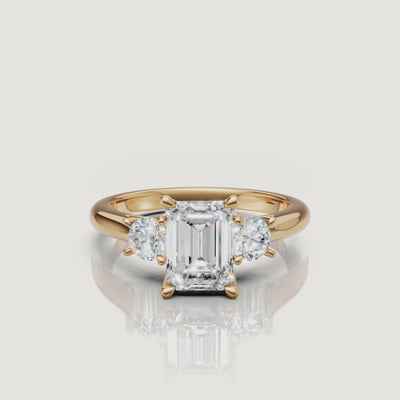 360-degree video showcase of the Raul Diamonds emerald cut three-stone ring in yellow gold, highlighting the hall-of-mirrors effect and the sparkle of the round side diamonds.