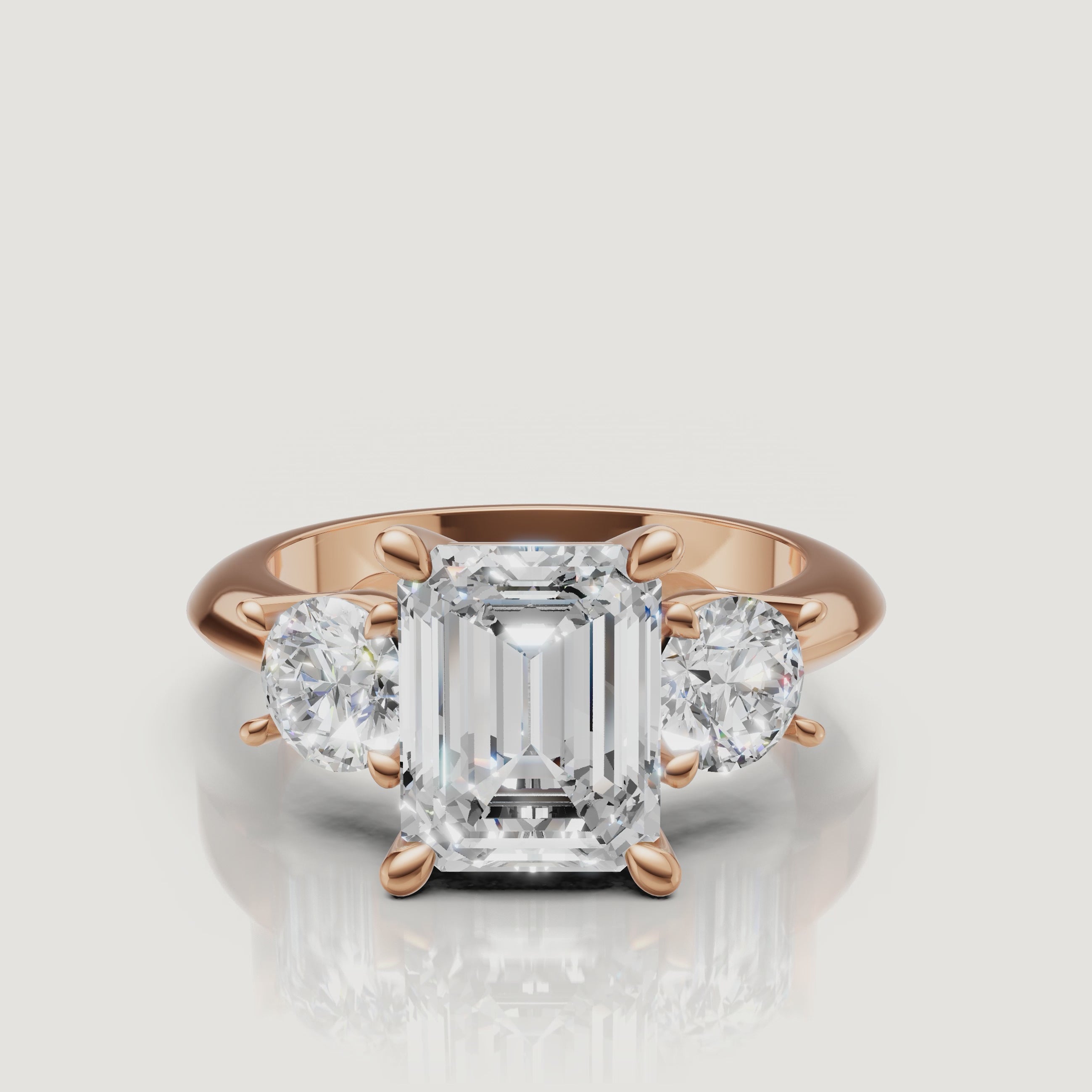 Cinematic close-up of the Vivienne rose gold emerald trilogy ring, focusing on the warm blush metal and the high-clarity step-cut facets of the center diamond.