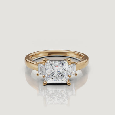 Cinematic 360-degree video showcase of the Raul Diamonds princess cut three-stone engagement ring in 18k yellow gold, highlighting the sparkle of the center diamond and the sleek emerald side stones.