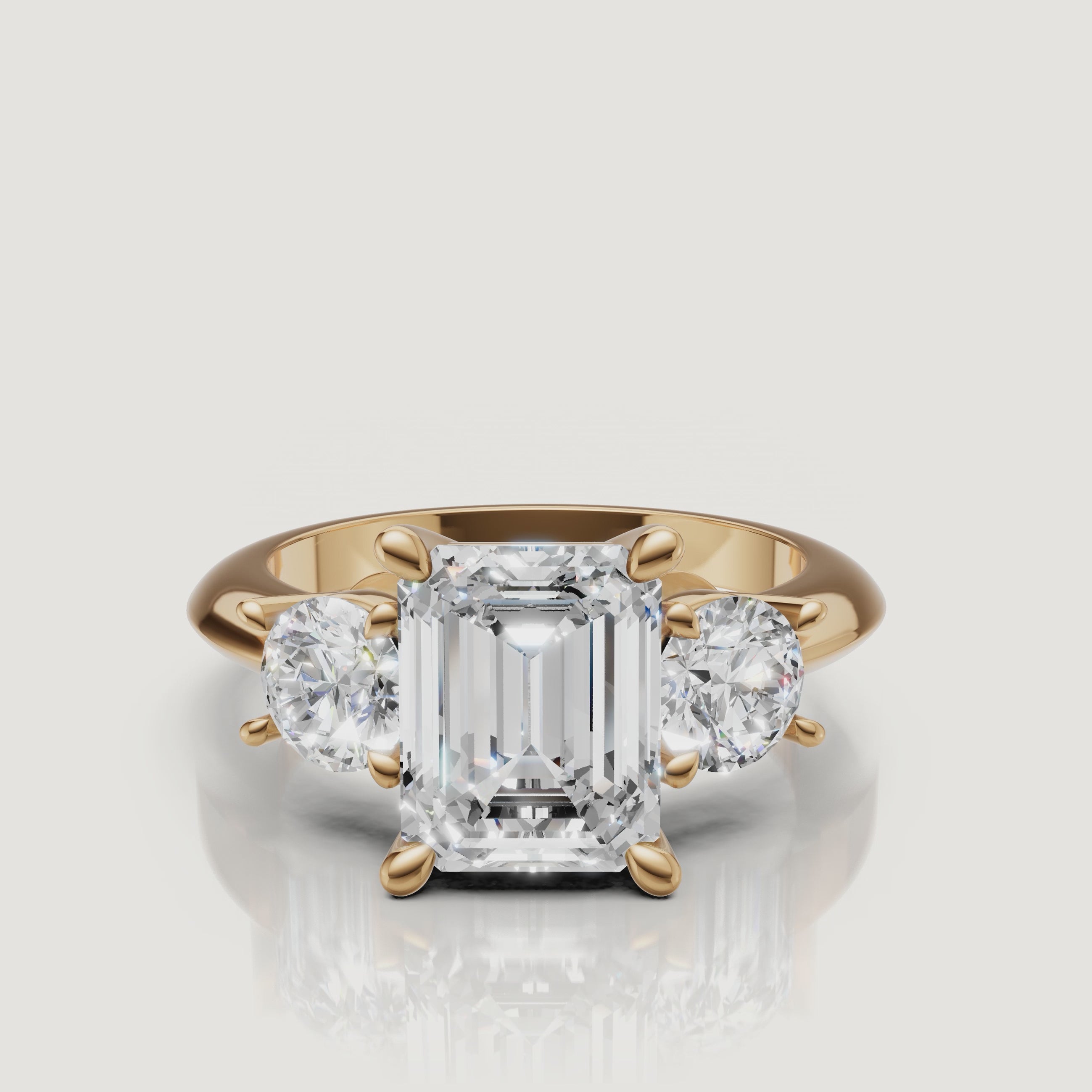 360-degree video showcase of the Raul Diamonds emerald cut three-stone ring in yellow gold, highlighting the hall-of-mirrors effect and brilliant round side diamonds.