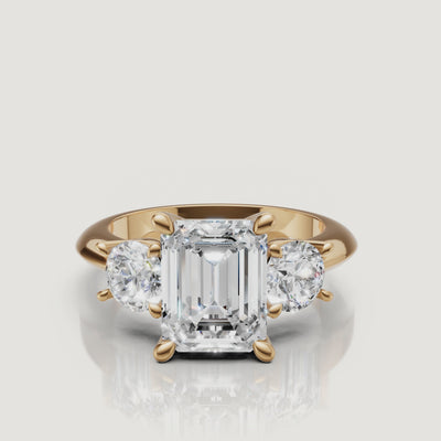 360-degree video showcase of the Raul Diamonds emerald cut three-stone ring in yellow gold, highlighting the hall-of-mirrors effect and brilliant round side diamonds.